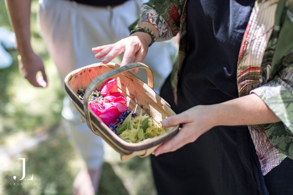 Person holding a small wooden basket filled with freshly picked flower petals.