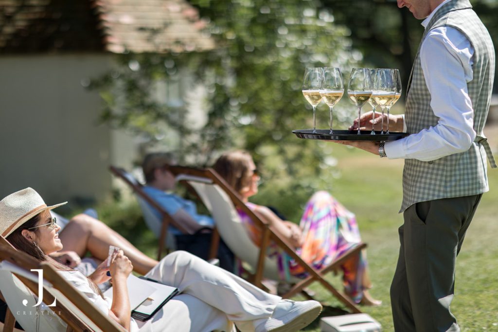 Hospitality server carrying a tray of sparkling wine for guests relaxing outdoors.