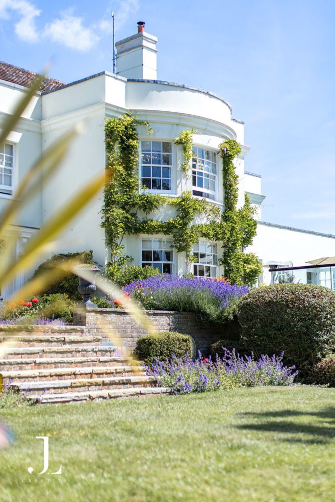 Sunlit white facade of Knepp Estate house framed by lavender gardens and stone steps.