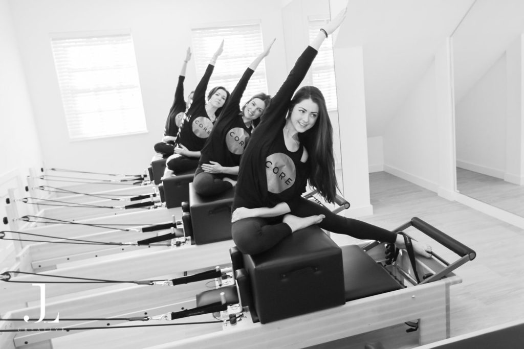 Clients practicing side stretches on reformer boxes during Pilates studio photography in Surrey.
