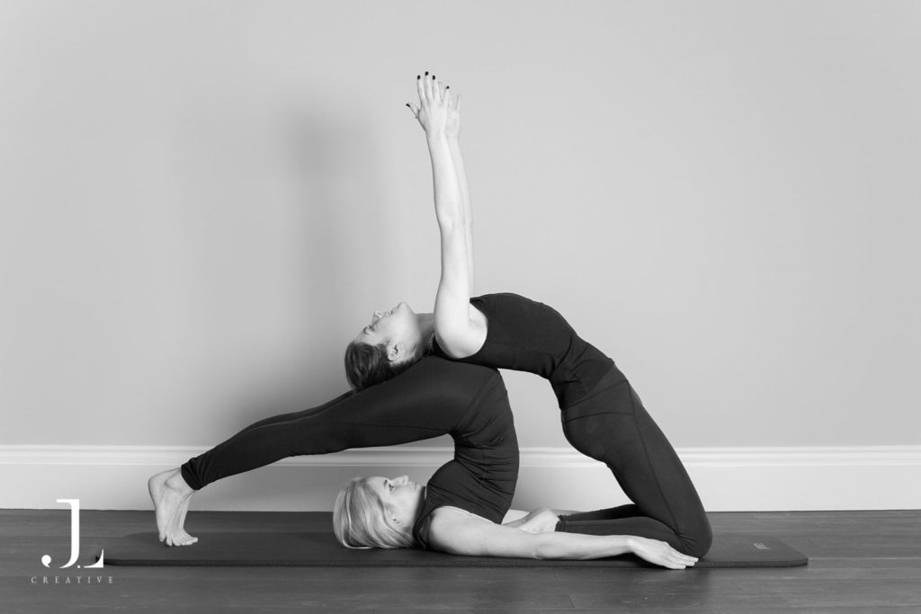 Two women performing an advanced partner backbend stretch during Pilates studio photography in Surrey.