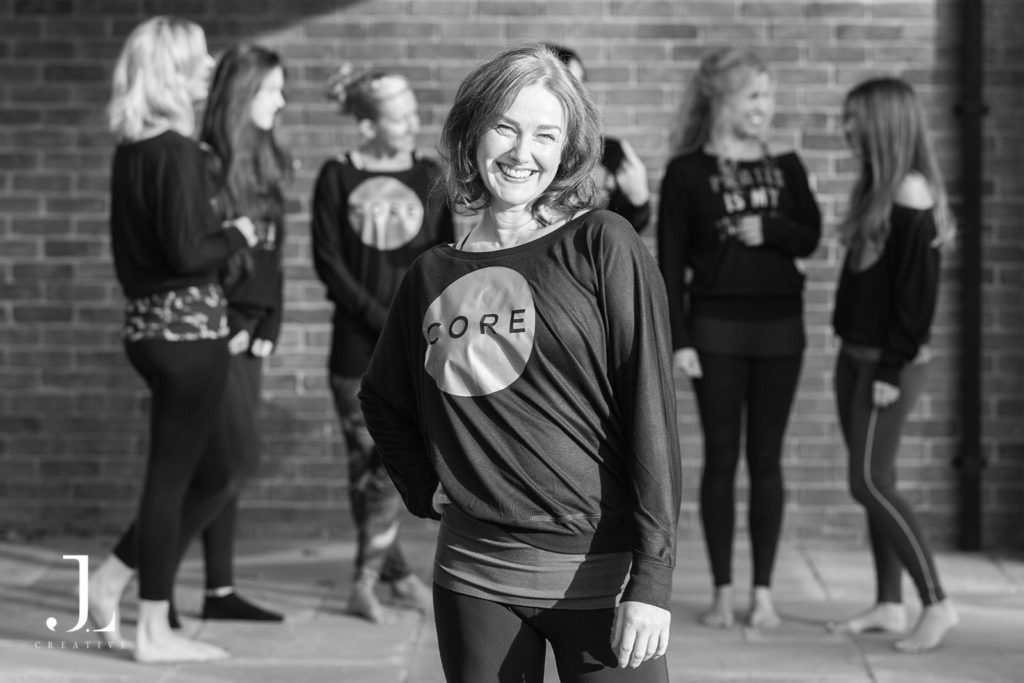 Solo instructor portrait with a group conversing in the background during Pilates studio photography in Surrey.