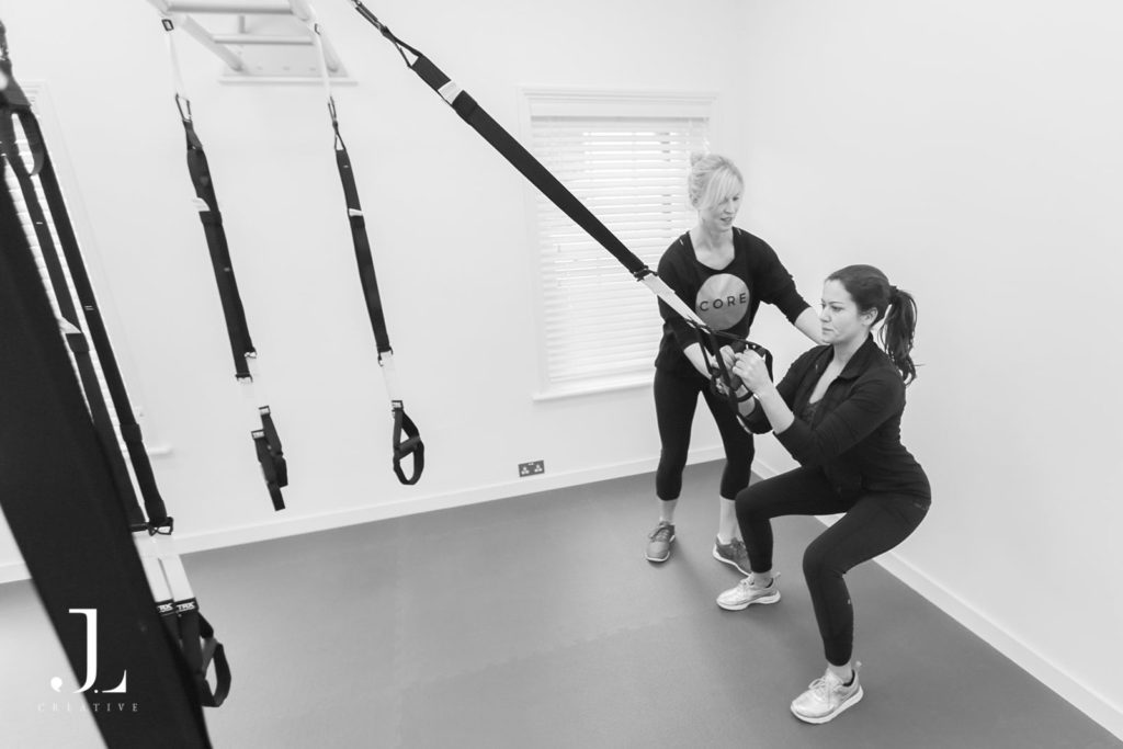 Instructor guiding a client through suspension squat training during Pilates studio photography in Surrey.